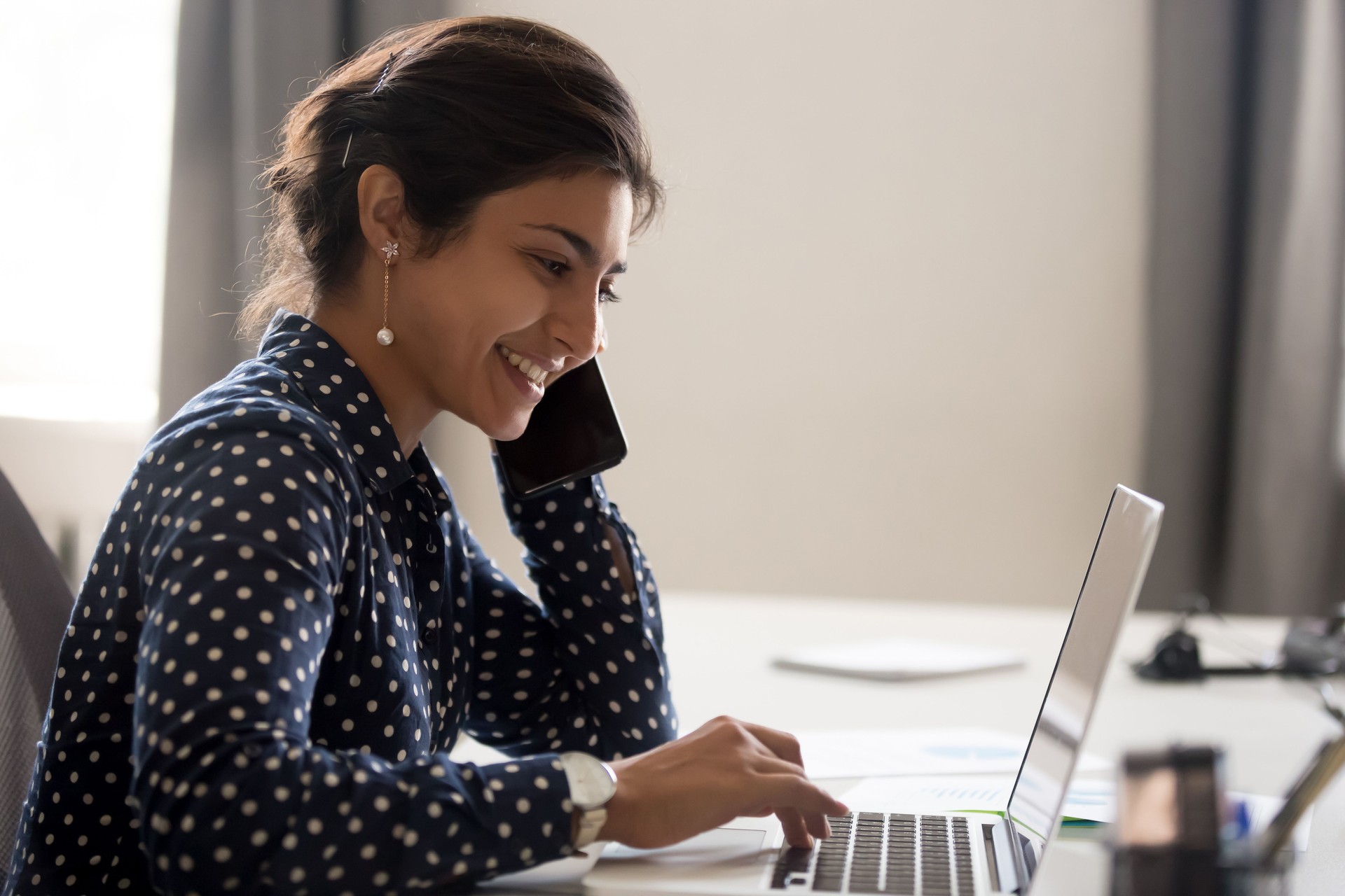Employé de sourire travaillant sur l'ordinateur portatif parlant au-dessus du téléphone